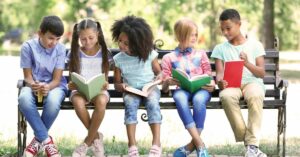 five kids sit on a bench reading books