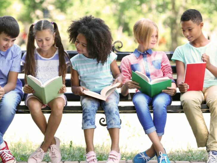 five kids sit on a bench reading books