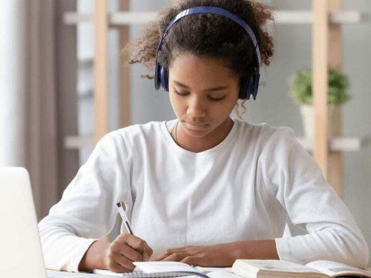a girl wears headphones and writes in front of a computer