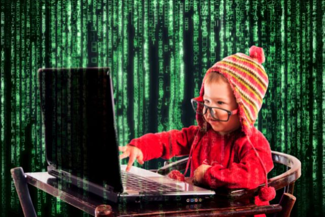 a toddler wearing a toque and glasses types on a laptop