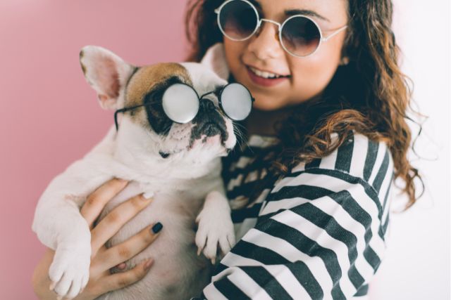 a woman holds a dog. Both wear glasses. 