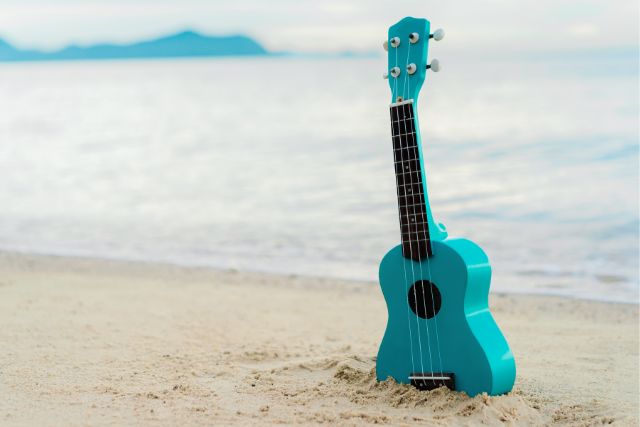 a green ukulele sticks out of the sand