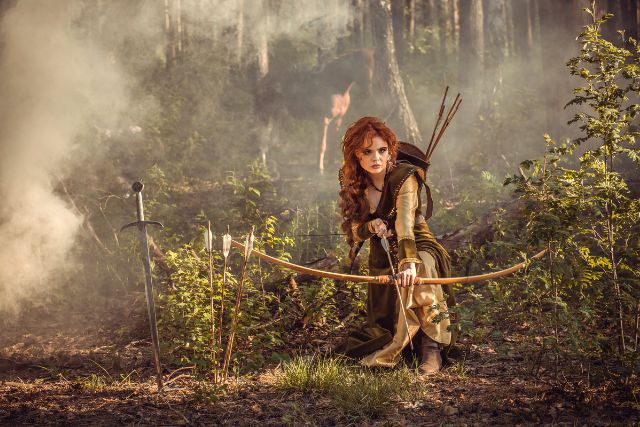 a woman in the woods shoots a bow and arrow