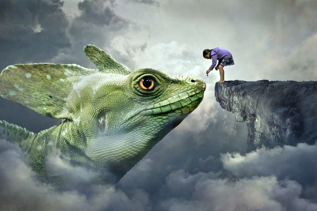 a girl standing on the tip of a cliff pats the nose of a giant lizard